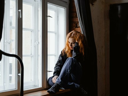 A woman sat on a windowsill with her elbow resting on her knee