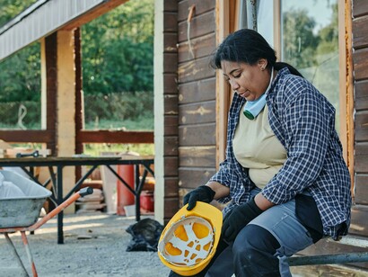 A woman in a yellow hard hat and black-and-white plaid shirt works with focus, striving to make a living