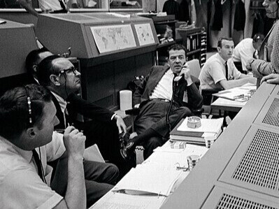 Centre de contrôle de mission dans le centre spatial Johnson, à Houston, au Texas, États-Unis en 1966. Autour du vol Gemini-11, ingénieurs et astronautes échangent en pleine concentration. Christopher C. Kraft Jr., Charles W. Mathews et Donald K. Slayton coordonnent les opérations aux côtés des astronautes William A. Anders et John W. Young, au cœur de la prise de décision spatiale. Photo prise pas la NASA
