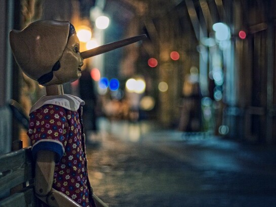 Una statua di Pinocchio, seduta su una panchina in una via notturna illuminata da luci soffuse