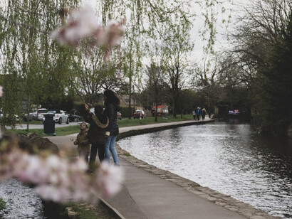 A couple standing by the river, with a white cherry blossom tree in full bloom, in Bourton-on-the-Water, Cotswolds