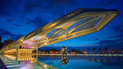 O Museu do Amanhã se projeta sobre o espelho d’água da Praça Mauá, iluminado contra o céu azul do início da noite. A arquitetura de Santiago Calatrava transforma o edifício em um dos símbolos mais marcantes do Rio de Janeiro contemporâneo