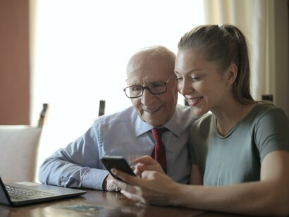 A grandfather and granddaughter using a laptop and phone together 