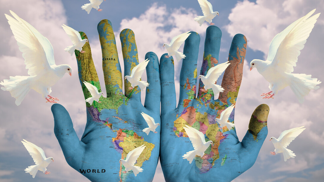 A white dove rests gently above a pair of open hands holding a world map, symbolizing global peace and harmony