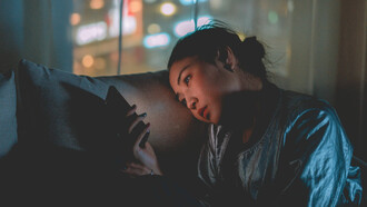 A woman lying on a pillow looking at her phone with sadness