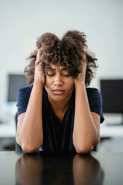 Portrait of a tired woman sitting at a desk, touching her face while lost in deep thought