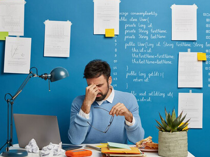 An unhappy male developer in glasses sits at his desk, overwhelmed by a tough workday and coding frustrations