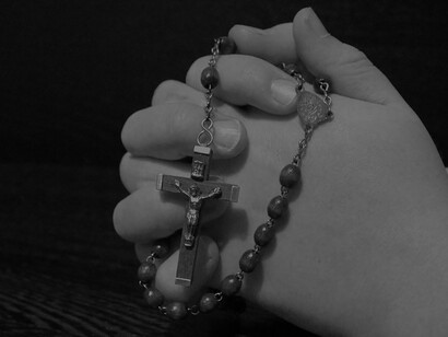 Amidst the sacred setting of the church, a man bows his head in prayer, his hands holding a cross, symbolizing a profound spiritual connection