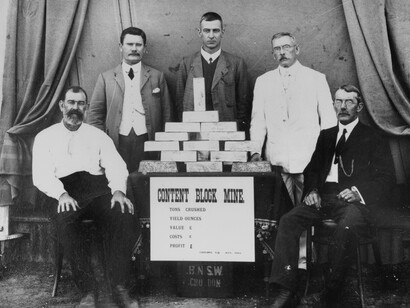 Grupo de hombres reunidos alrededor de una mesa llena de lingotes de oro, 1912