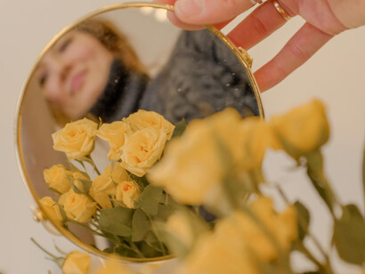 A woman in grey sweatear holding a bunch of flower and smiling at the mirror