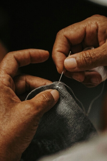 Em close, dedos conduzem a linha através da trama do tecido. A agulha atravessa o tecido guiada por mãos atentas. Cada ponto é uma pequena aposta na continuidade. Há coisas que não precisam de ser substituídas, apenas cuidadas. Cada ponto é uma pequena aposta na continuidade