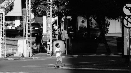 Sozinho, um menino atravessa a rua em direção à parte escura da imagem, deixando para trás a área iluminada onde seus passos ainda podem ser vistos. A cena evoca a trajetória de uma infância marcada não por uma perda, mas por uma ausência que já estava presente desde o nascimento com a ausência de um pai que nunca chegou a ocupar seu lugar