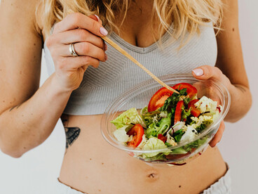 A fit woman enjoys a fresh vegetable salad while tracking her calorie intake and maintaining healthy eating habits