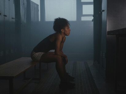 A woman standing in a professional locker room, with empty benches and dramatic lighting emphasizing a quiet, reflective atmosphere