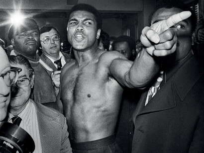 Manhattan, New York City, New York / January 23, 1974. Surrounded by press and bodyguards, Muhammad Ali gestures before brawling with Joe Frazier at the New York studio of ABC during the weigh-in process. Both were fined $5,000. Ali went on to box Frazier on January 28, won the fight and retained his NABF title.