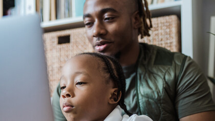 Pai com o seu filho no colo o distrai com jogos no computador enquanto atualiza os e-mails