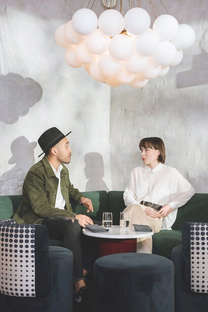 During their speed date, a woman donning a crisp white shirt and a man sporting a stylish hat share genuine laughter, clearly relishing their time together