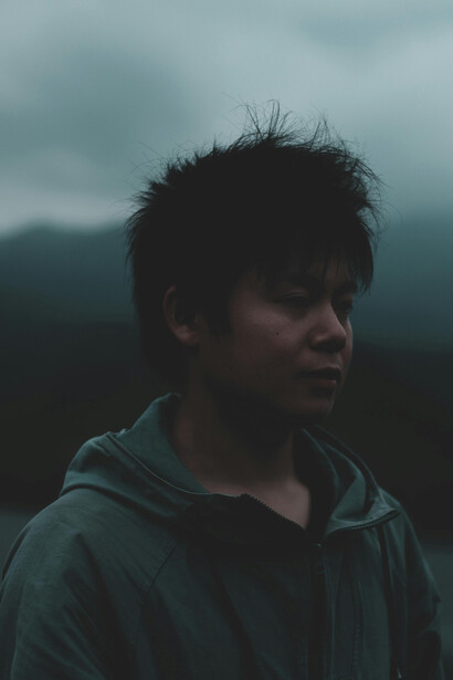 In a dense, fog-covered forest, a hooded man stands still—lost in thought, consumed by mental haze