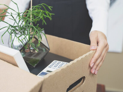 Capture the stark reality of an economic crisis and mass layoffs through imagery of a person carrying a box, illustrating the tangible consequences of inflation