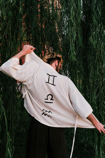 Un muchacho frente a una planta y con signos zodiacales en su ropa