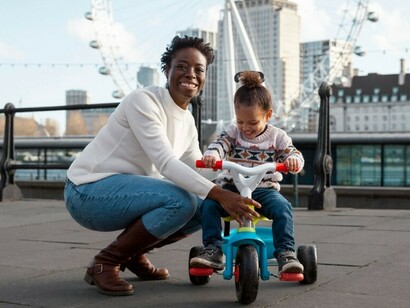 A woman watches as her child pedals a tricycle through the park