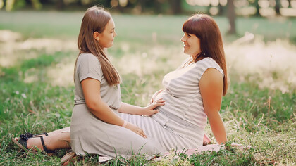 A woman is touching the belly of another pregnant woman, helping her