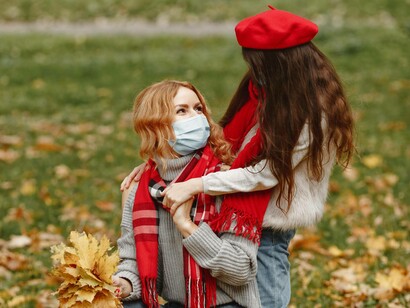 A mother playing with her daughter in the park while wearing a mask
