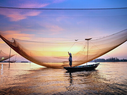 Fishing nets stretching across calm waters at sunset, symbolising the fragile lines that connect memory, labour, and belonging