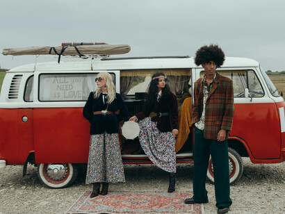 Young people standing beside a red Volkswagen van on the road, evoking a nostalgic, free-spirited mood
