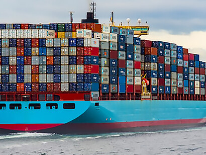A cargo ship, painted in vivid blue and red, sails across the open sea under the bright daylight