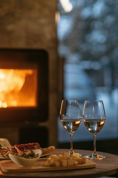 Wine glasses and food arranged on a wooden table create a cozy atmosphere by the fireplace