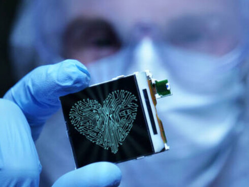 An ultra-modern electronics manufacturing facility where a design engineer in a sterile coverall holds a microchip displaying futuristic holographic symbols, representing organ-on-chip technology