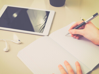 Mujer escribe en un cuaderno de notas junto a una tableta