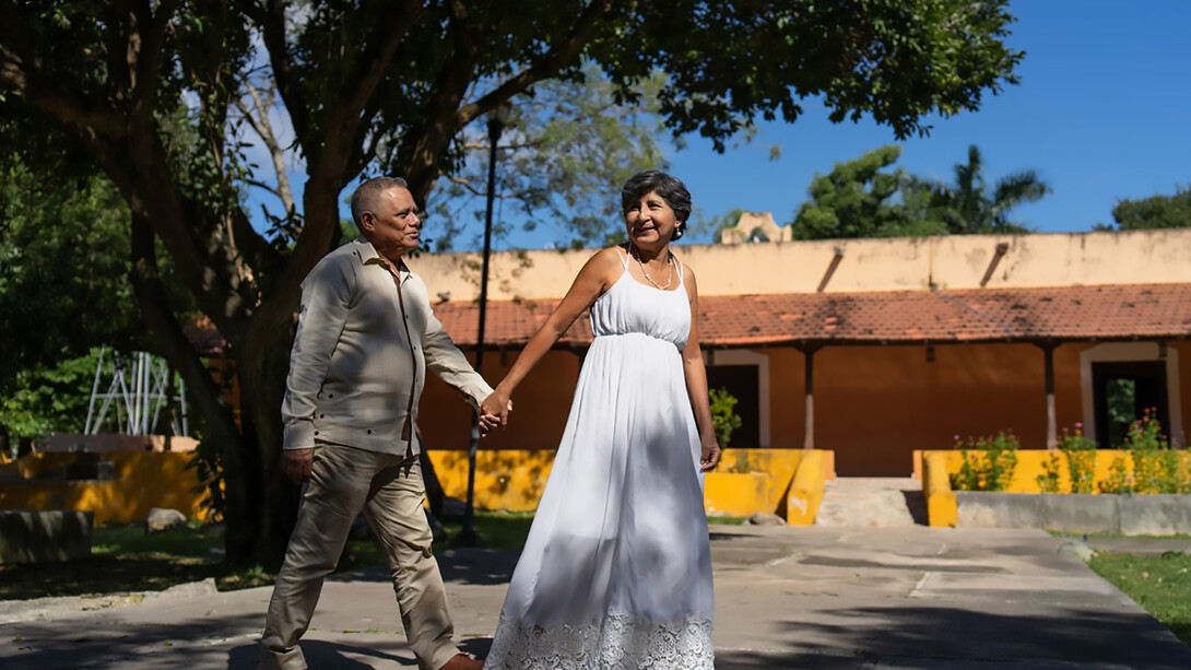 A happy elderly Indian couple stands smiling outside their home, radiating warmth and togetherness