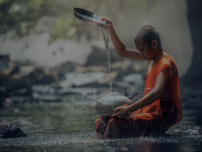 A young monk boy carefully filling cups with river water