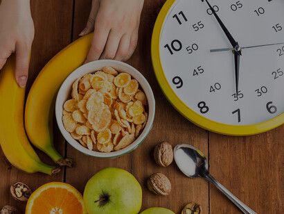 A depiction of intermittent fasting: a healthy homemade breakfast of muesli, apples, fresh fruits, and walnuts, with a clock on the table