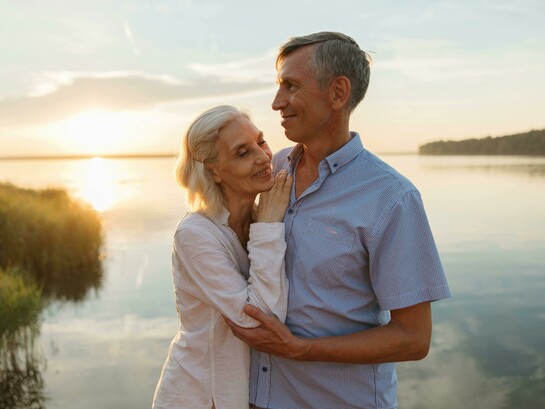 A sweet couple standing by the water at sunset, sharing a peaceful moment together