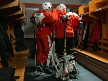 Hockey teammates standing shoulder to shoulder with their arms around one another, reflecting solidarity within a goal-oriented team