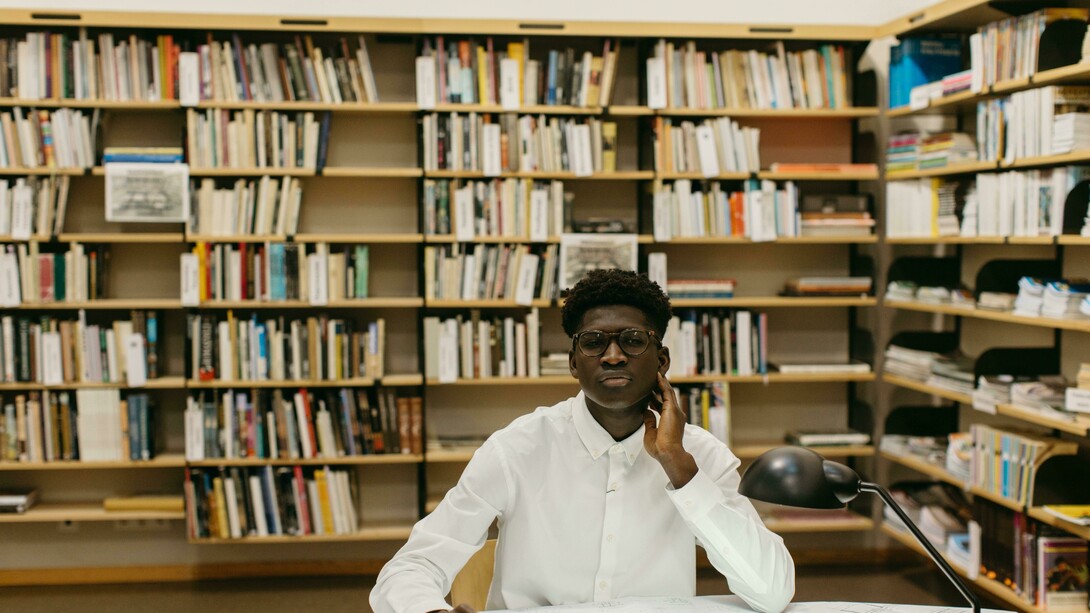 A male architecture student sitting at a table in the library, focused on his studies
