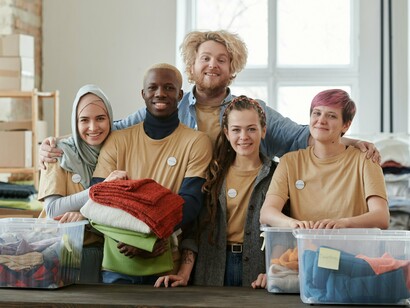 Voluntários posam juntos diante de caixas com roupas organizadas para doação. A atuação coletiva e a organização de recursos são parte da estrutura necessária para ampliar a capacidade de ação das organizações do terceiro setor