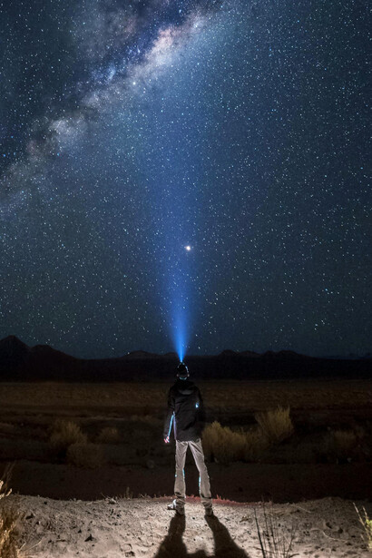 Hombre apuntando su linterna al cielo estrellado. Todas las leyes de la naturaleza son la réplica de la esencia universal