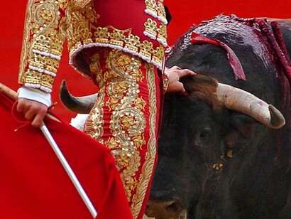 Un torero detiene al toro con una mano mientras sujeta la muleta y la espada con la otra