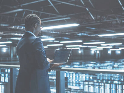 An IT specialist analyzes data on a tablet computer while overseeing a large server farm in a cloud computing facility, ensuring optimal performance of quantum information systems and stochastic resonance technologies