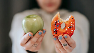 Woman holding an apple in one hand and a donut in the other emphasizes the importance of a preventive diet against cancer