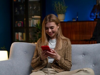 A woman relaxing on her couch at home, focused on her phone, reflecting the impact of digital media and online influence
