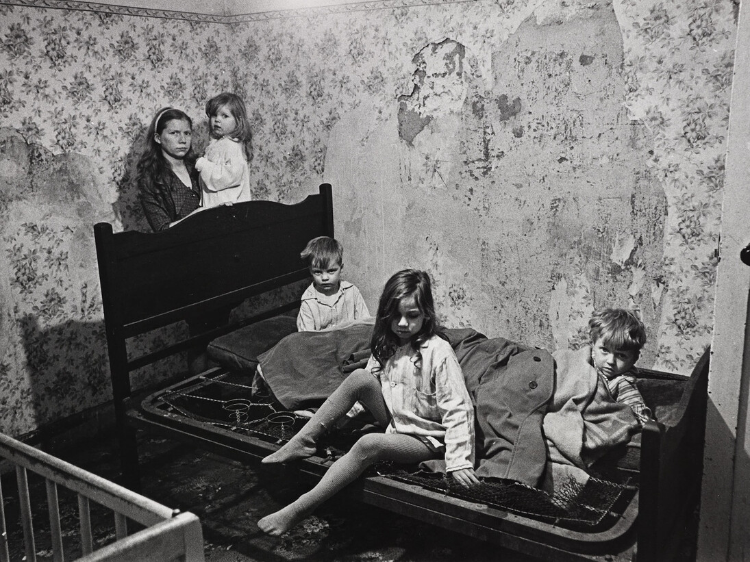 Mr and Mrs M and their four children lived in a council owned house in Vincent Crescent, Balsall Heath. Apart from the poor state of the property – no bathroom, no hot water, outside lavatory, inside walls running with damp – these children were sleeping in the middle of winter, on two sodden seat cushions covered by a couple of old ‘macs’, there was no heating in the room, the snow lay thick outside and the windows were broken. Birmingham, January 1969 © Nick Hedges / National Media Museum, Bradford
