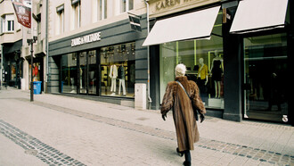 Stylish woman in a brown fur coat passing by the storefronts of high-end brands such as Zadig & Voltaire