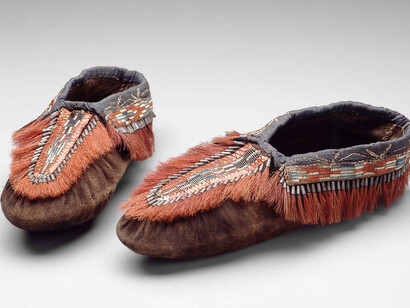 Moccasins, Huron-Wendat (Wyandot), Wendake, Quebec, early 19th century. Leather (probably moose or deer skin), woven dyed porcupine quills, bast fiber thread, plain weave silk ribbon, dyed hair tufts (probably moose), tinned sheet iron cones, napped plain weave wool backing. Gift of Miss Ellen A. Stone.