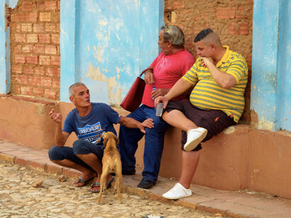 A group of locals sits on the corner of a lively South American street, sharing stories and laughter, embodying the tight-knit sense of community that defines their neighbourhood