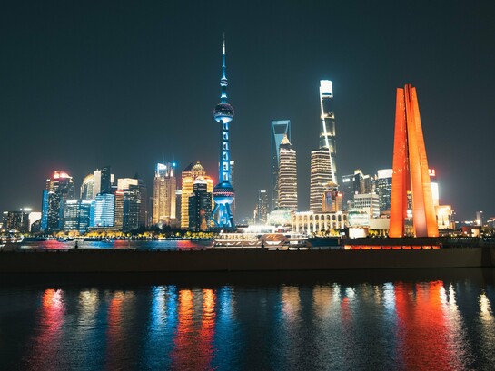 As luzes de Xangai iluminam o horizonte e se refletem nas águas da cidade durante a noite. A moderna paisagem urbana simboliza a retomada do protagonismo econômico chinês discutida ao longo do texto.